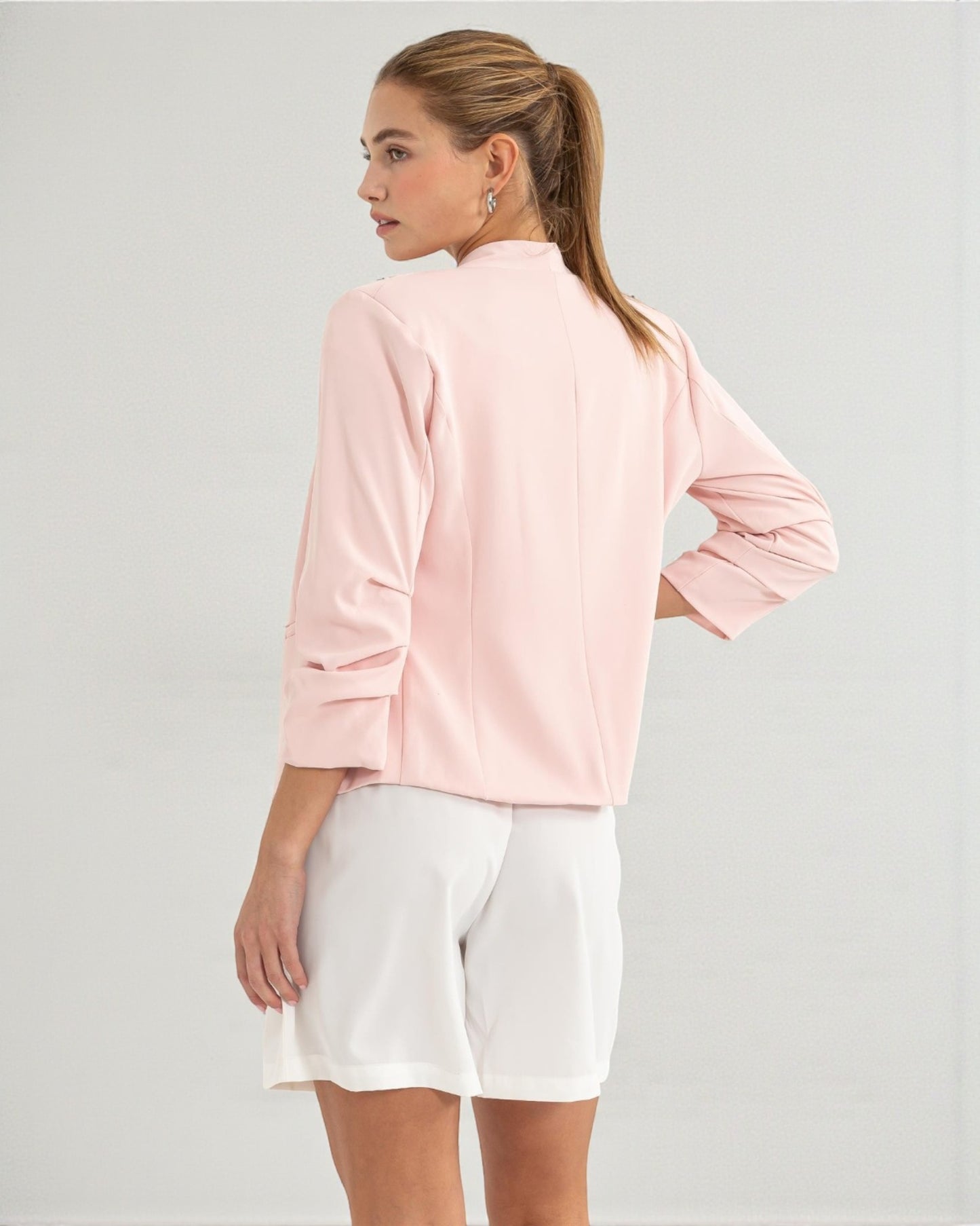 Woman wearing a light pink jacket and white shorts on a gray background