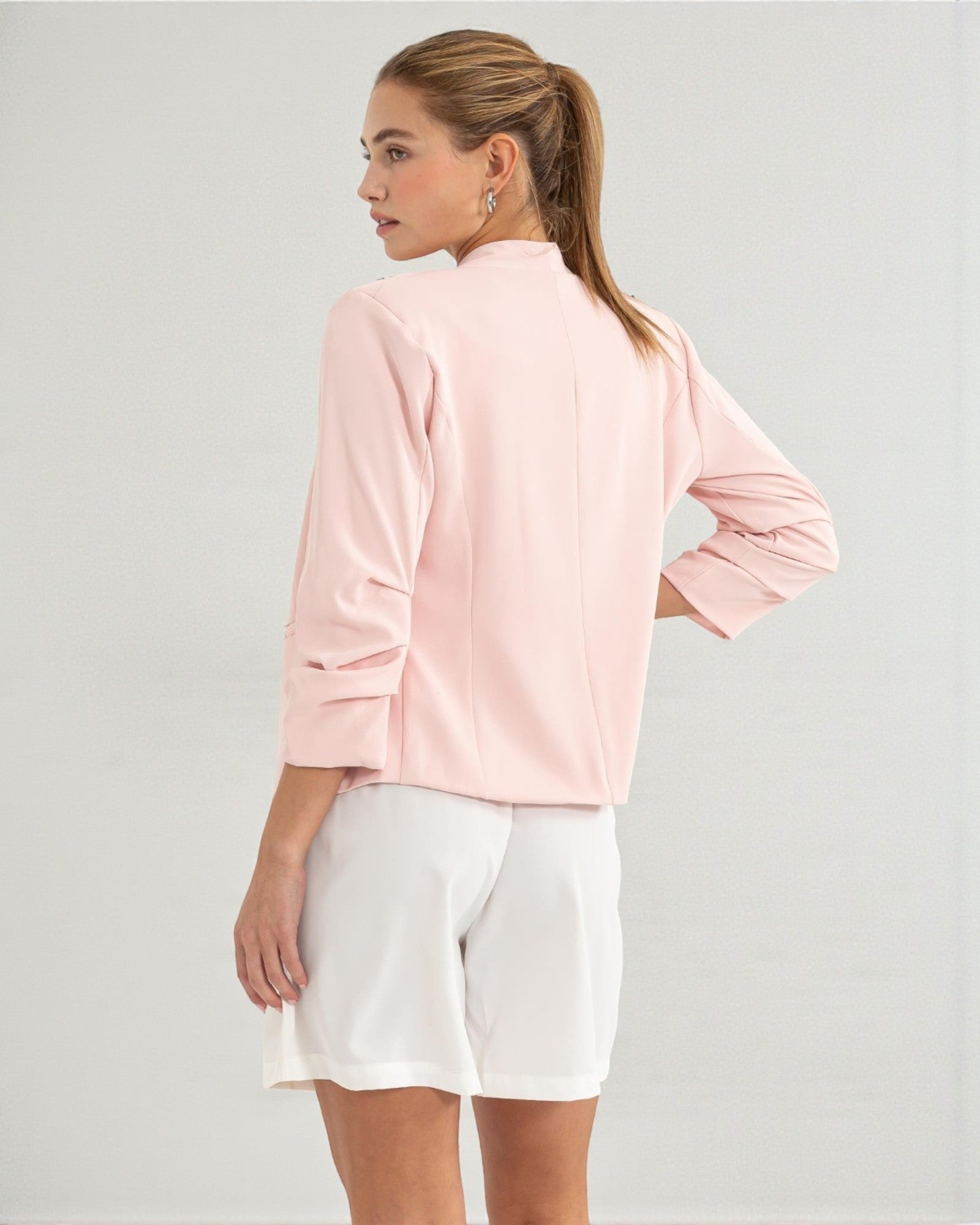 Woman wearing a light pink jacket and white shorts on a gray background