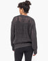 A woman viewed from the back wearing a dark charcoal gray open-knit sweater and black leggings against a plain white studio background.