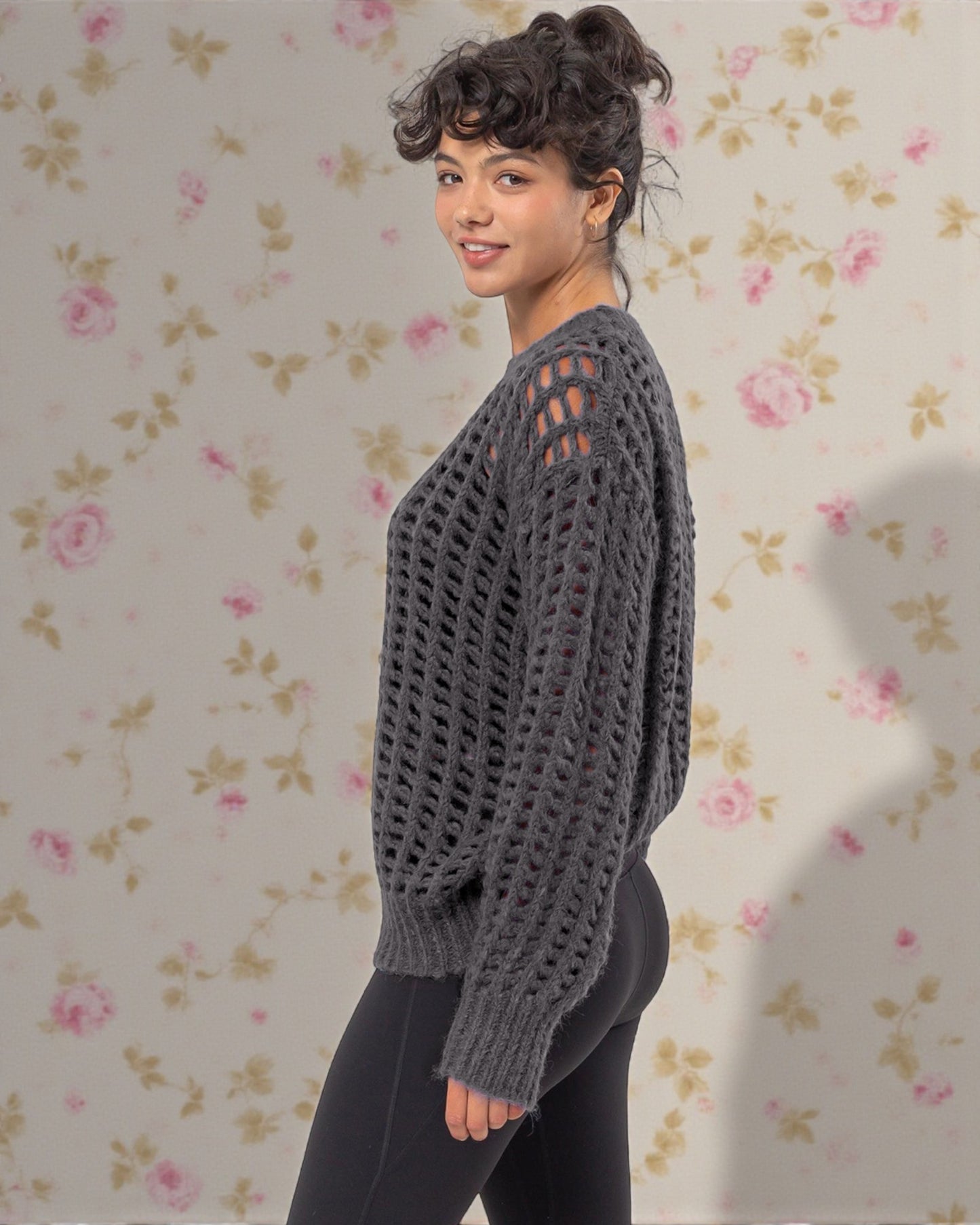 Woman wearing a gray knitted sweater against a floral wallpaper background