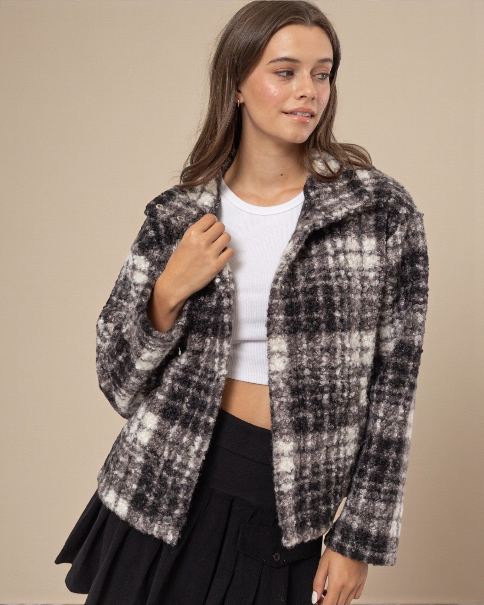 Woman wearing a plaid jacket over a white top and black skirt on a beige background