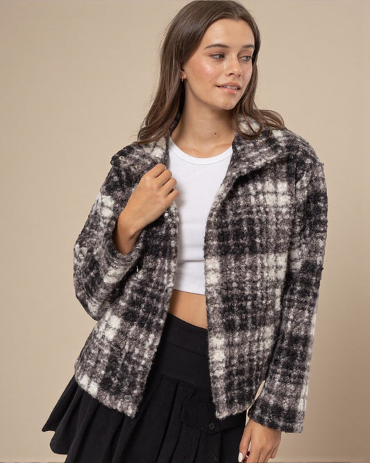 Woman wearing a plaid jacket over a white top and black skirt on a beige background