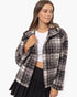 A woman modeling a fuzzy, cropped plaid jacket in black and off-white, worn over a white crop top and a black pleated skirt against a plain white background.