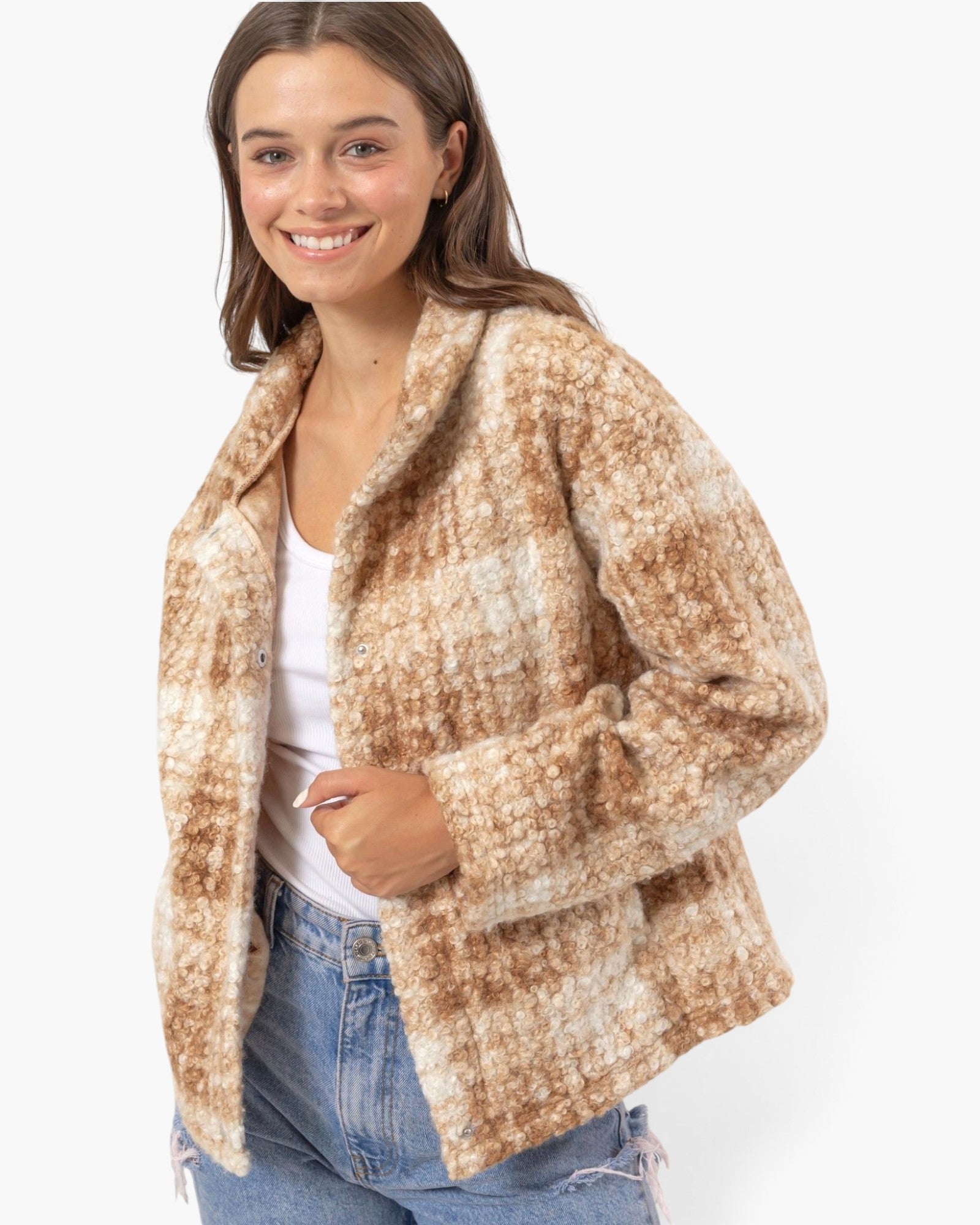 A woman wearing a fuzzy, textured open-front jacket in a mottled tan and cream plaid pattern, styled with a white tank top and blue jeans against a plain white background.
