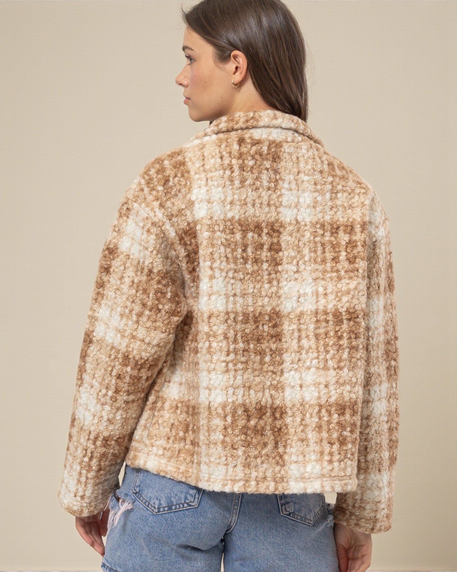 Person wearing a plaid jacket and jeans against a beige background