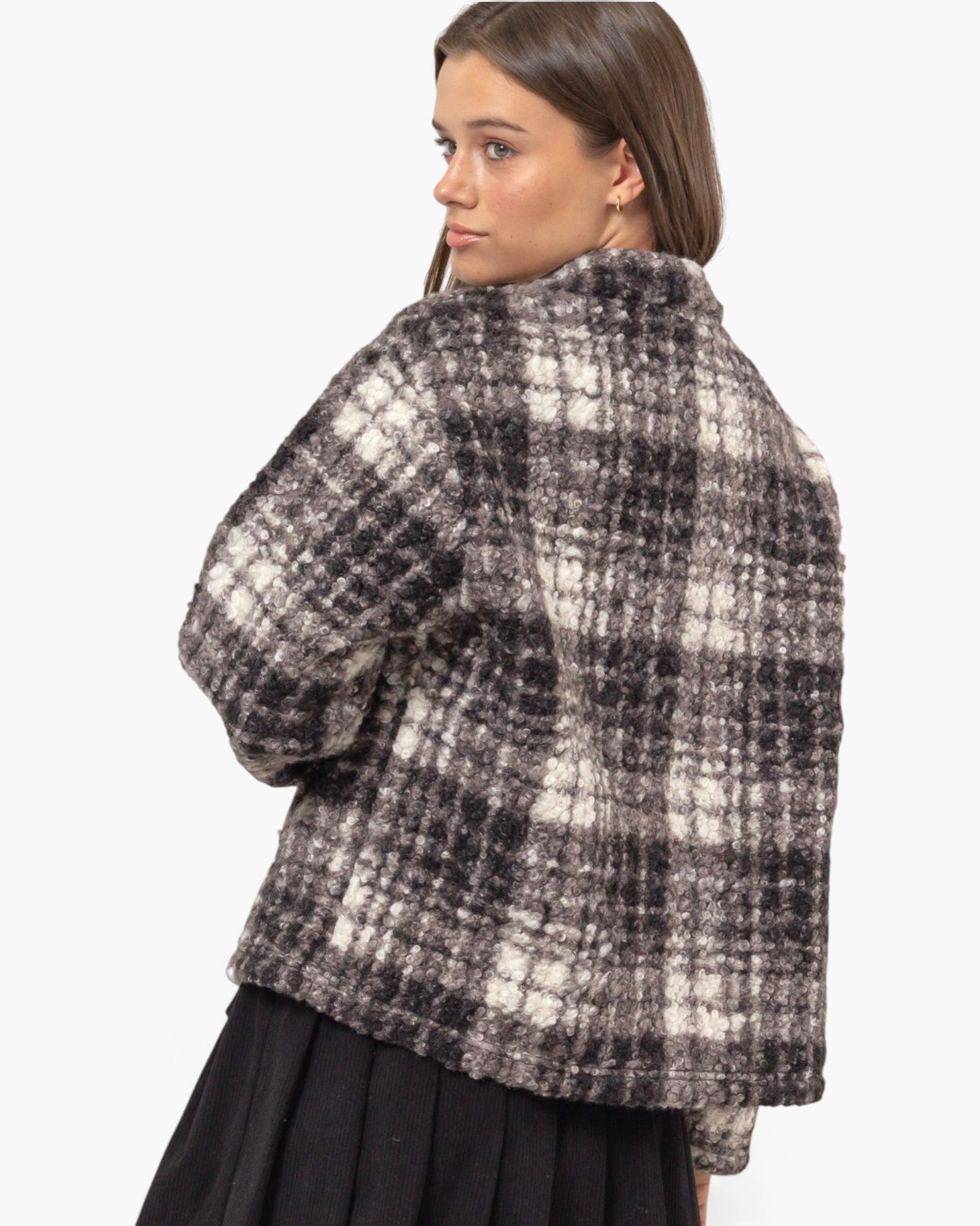 A woman shown from the back wearing a fuzzy black and off-white plaid cropped jacket over a black skirt, against a plain light gray studio background.