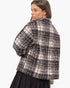 A woman shown from the back wearing a fuzzy black and off-white plaid cropped jacket over a black skirt, against a plain light gray studio background.