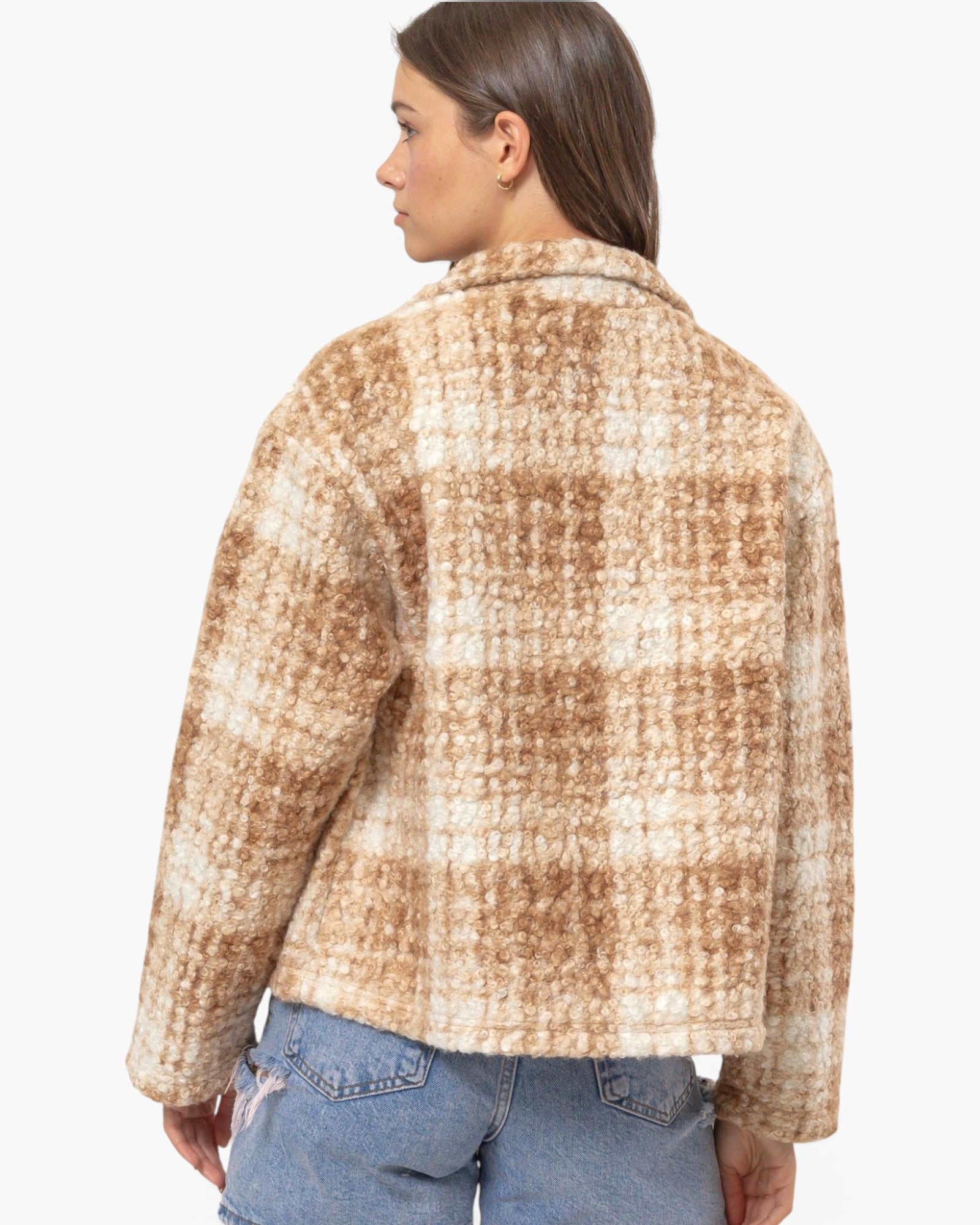 A woman shown from the back wearing a fuzzy cropped plaid jacket in beige and brown tones, paired with blue jeans, against a plain white studio background.