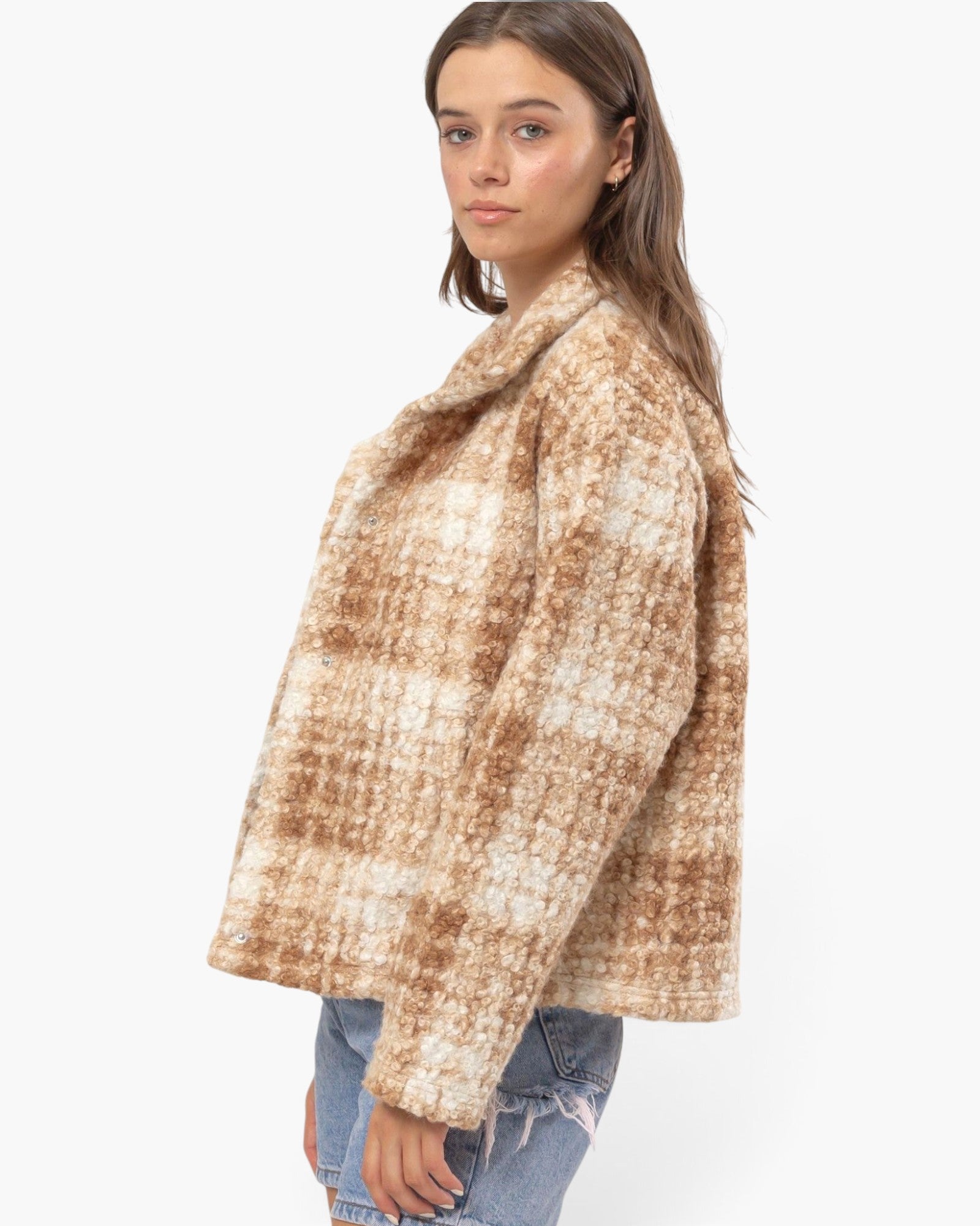 A woman wearing a fuzzy, oversized plaid jacket in beige and brown tones, paired with light-wash blue jeans, photographed against a clean white background.