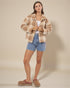 Woman wearing a plaid jacket, denim shorts, and brown shoes on a beige background