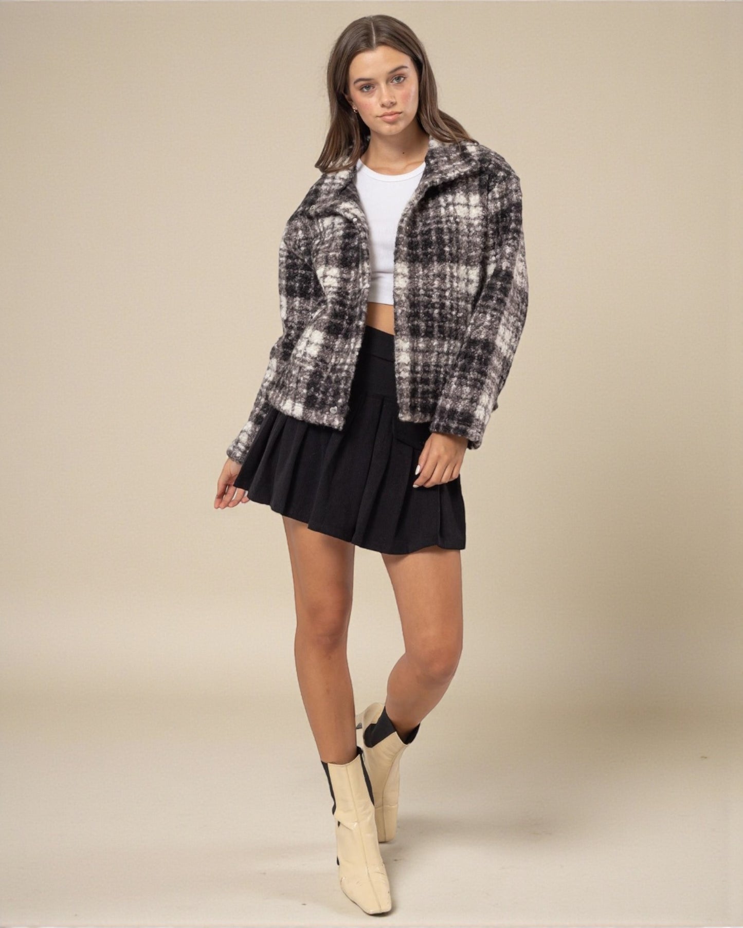 Woman wearing a plaid shirt, black skirt, and beige boots on a beige background