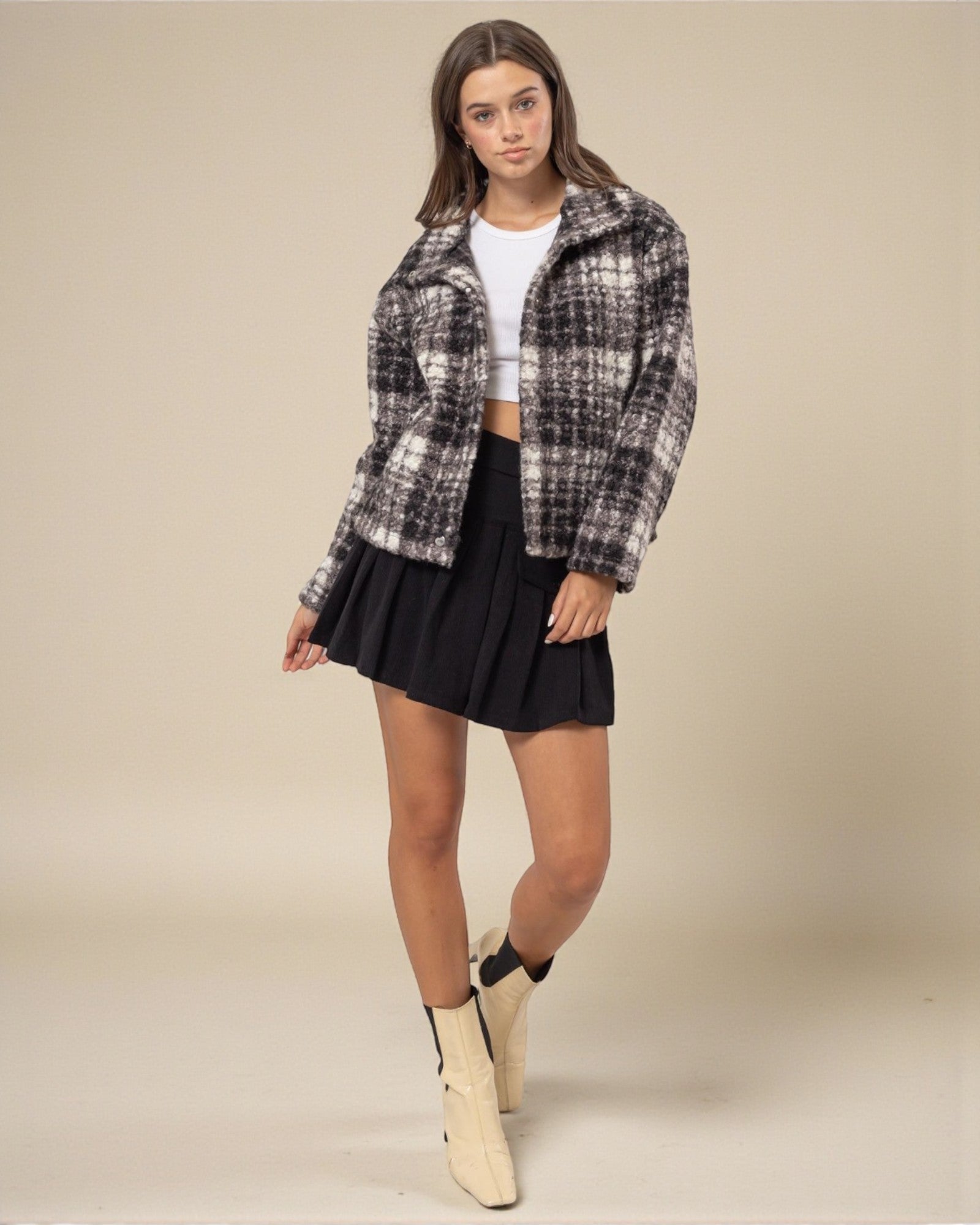 Woman wearing a plaid shirt, black skirt, and beige boots on a beige background