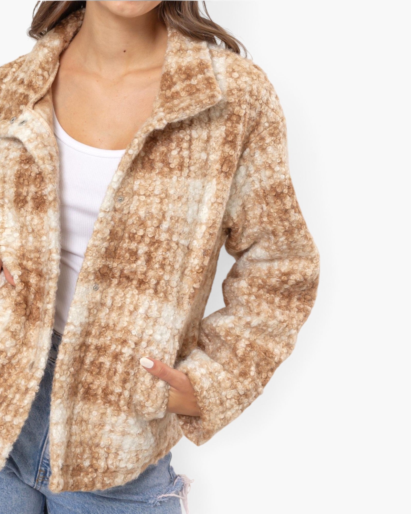 A close-up of a woman wearing a fuzzy, textured plaid jacket in shades of brown and cream, paired with a white tank top and blue jeans against a plain white background.