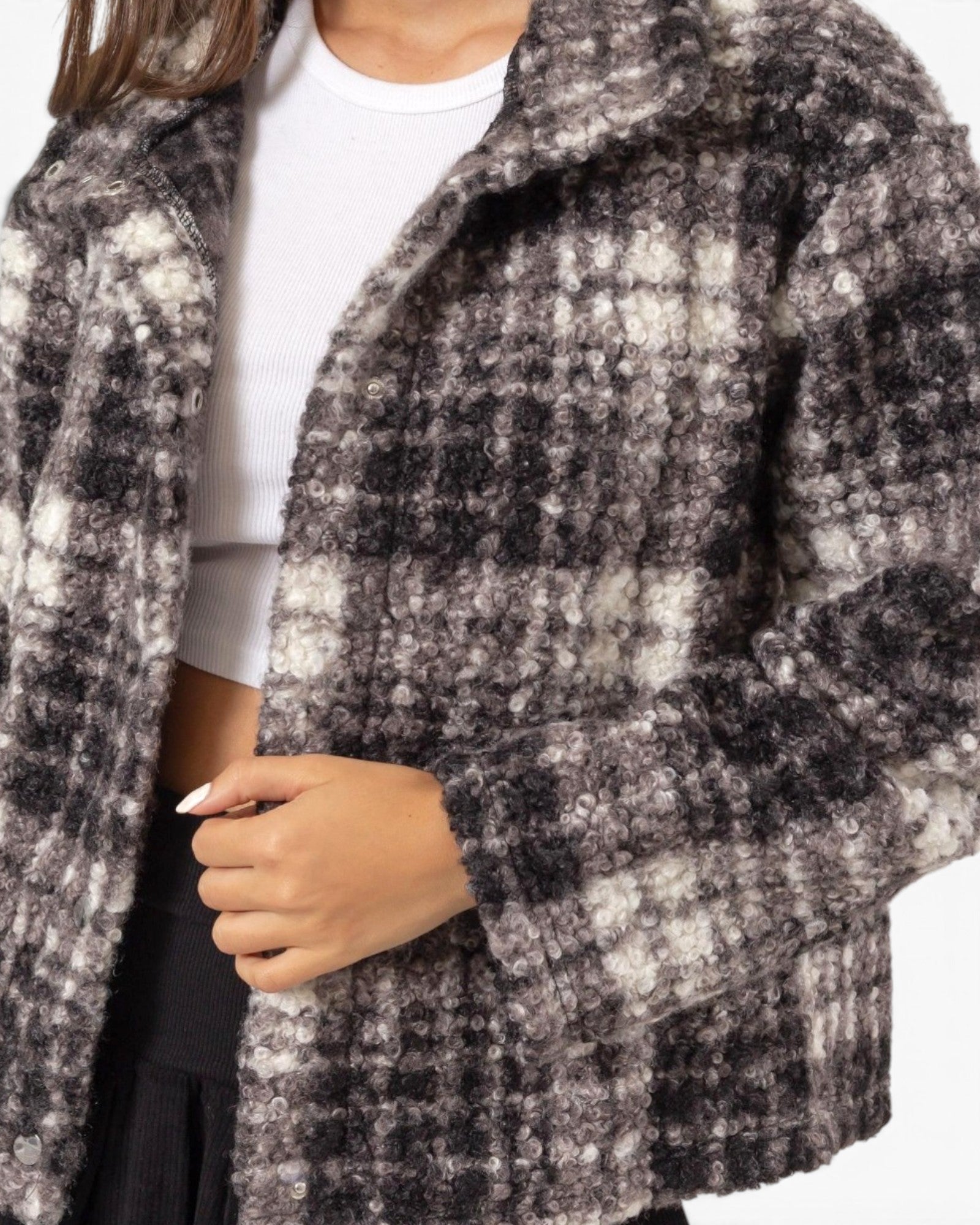 A close-up of a person wearing a fuzzy plaid coat in black, gray, and off-white, layered over a white ribbed crop top and dark bottoms.