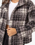 A close-up of a person wearing a fuzzy plaid coat in black, gray, and off-white, layered over a white ribbed crop top and dark bottoms.