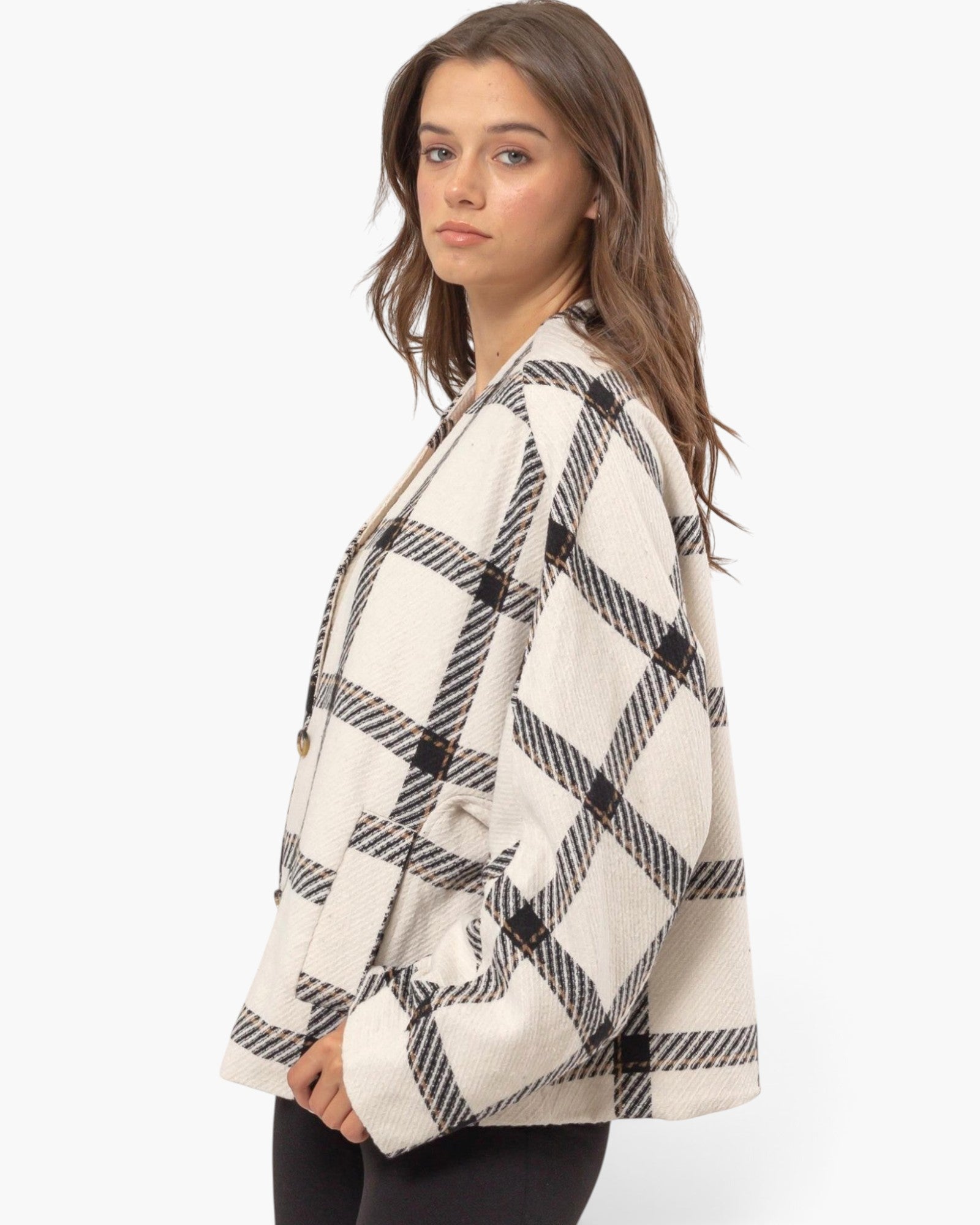A woman wearing a cropped, oversized plaid cardigan in cream and black, photographed against a clean white studio background.