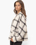 A woman wearing a cropped, oversized plaid cardigan in cream and black, photographed against a clean white studio background.