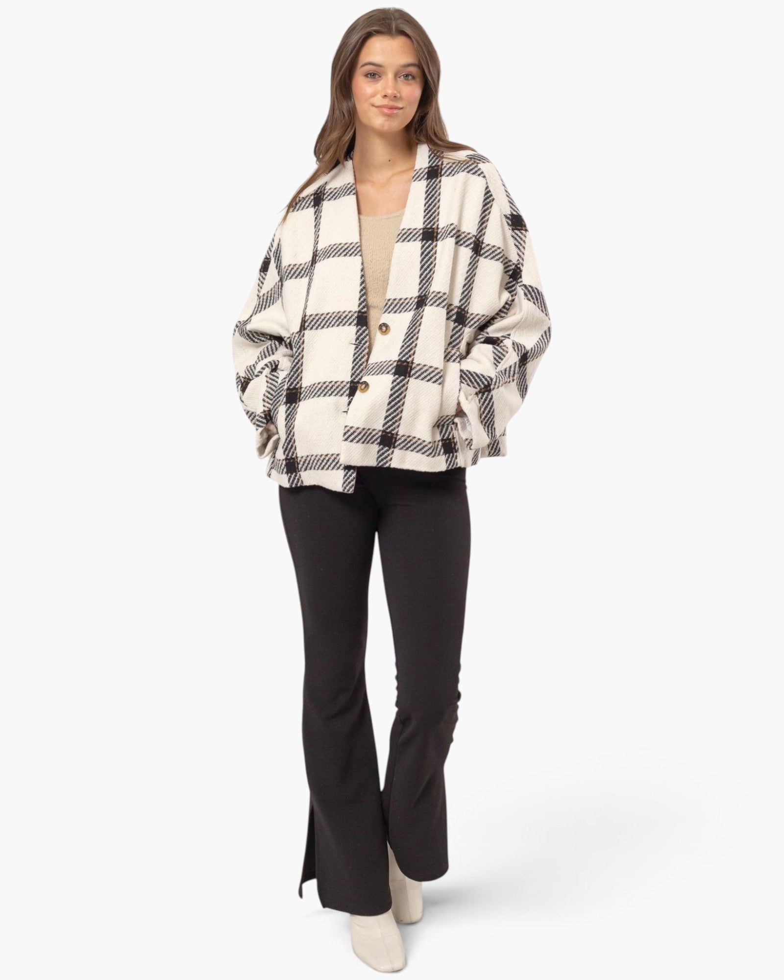 A woman modeling a black and off-white plaid button-up jacket with oversized sleeves, paired with black flared pants and off-white boots, against a plain white studio background.