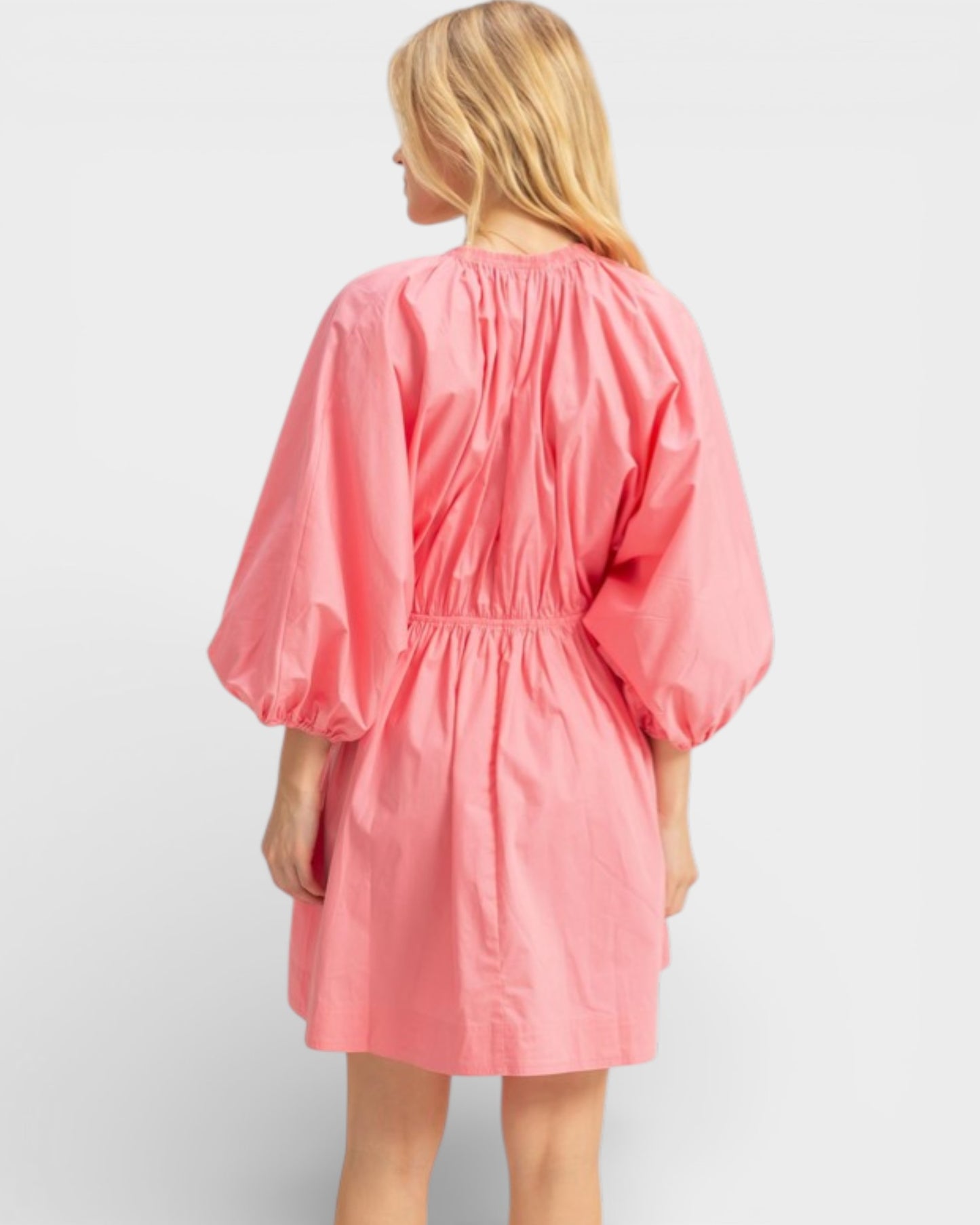 Woman wearing a pink dress with puff sleeves on a light gray background