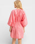 Woman wearing a pink dress with puff sleeves on a light gray background