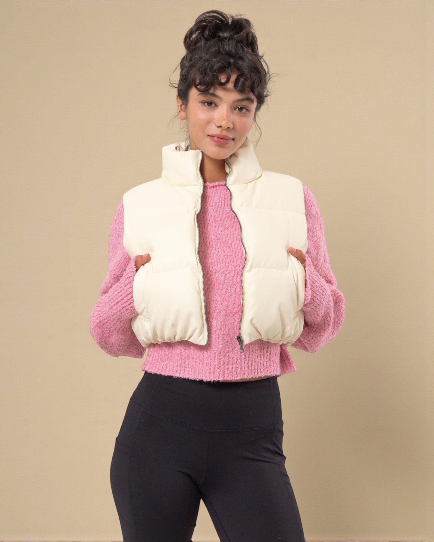 Person wearing a pink sweater and white puffer vest against a beige background