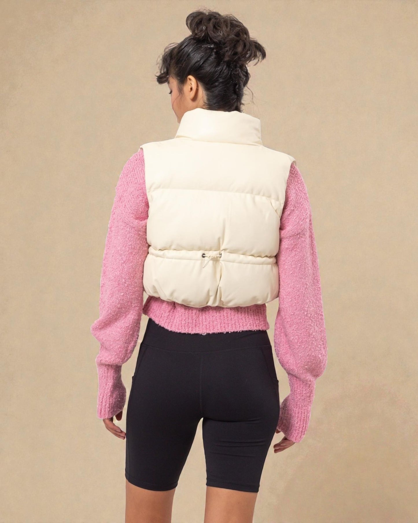 Person wearing a white puffer vest over a pink sweater on a beige background