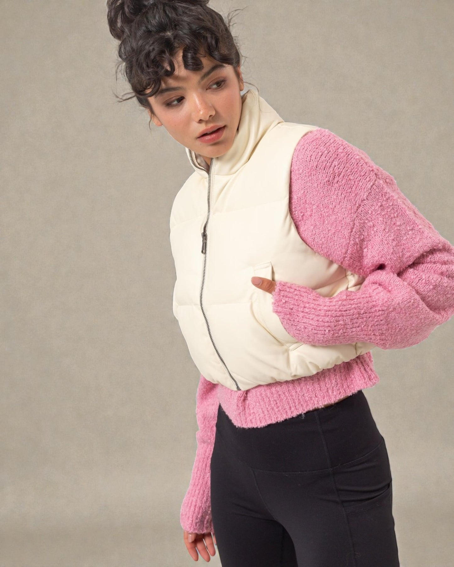 Person wearing a pink sweater over a white puffer vest on a neutral background