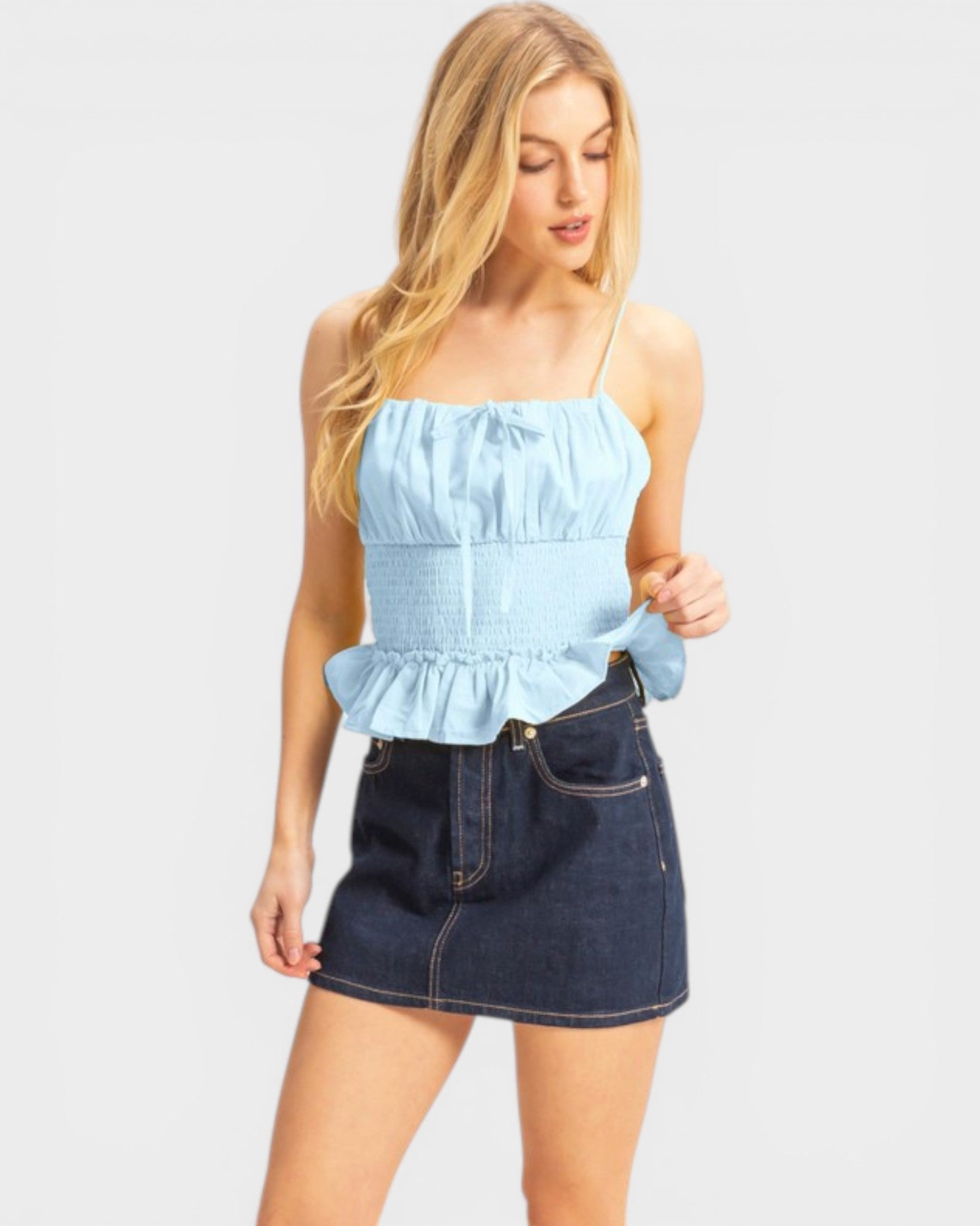 Woman wearing a light blue strapless top with ruffled details and a dark denim skirt on a white background.