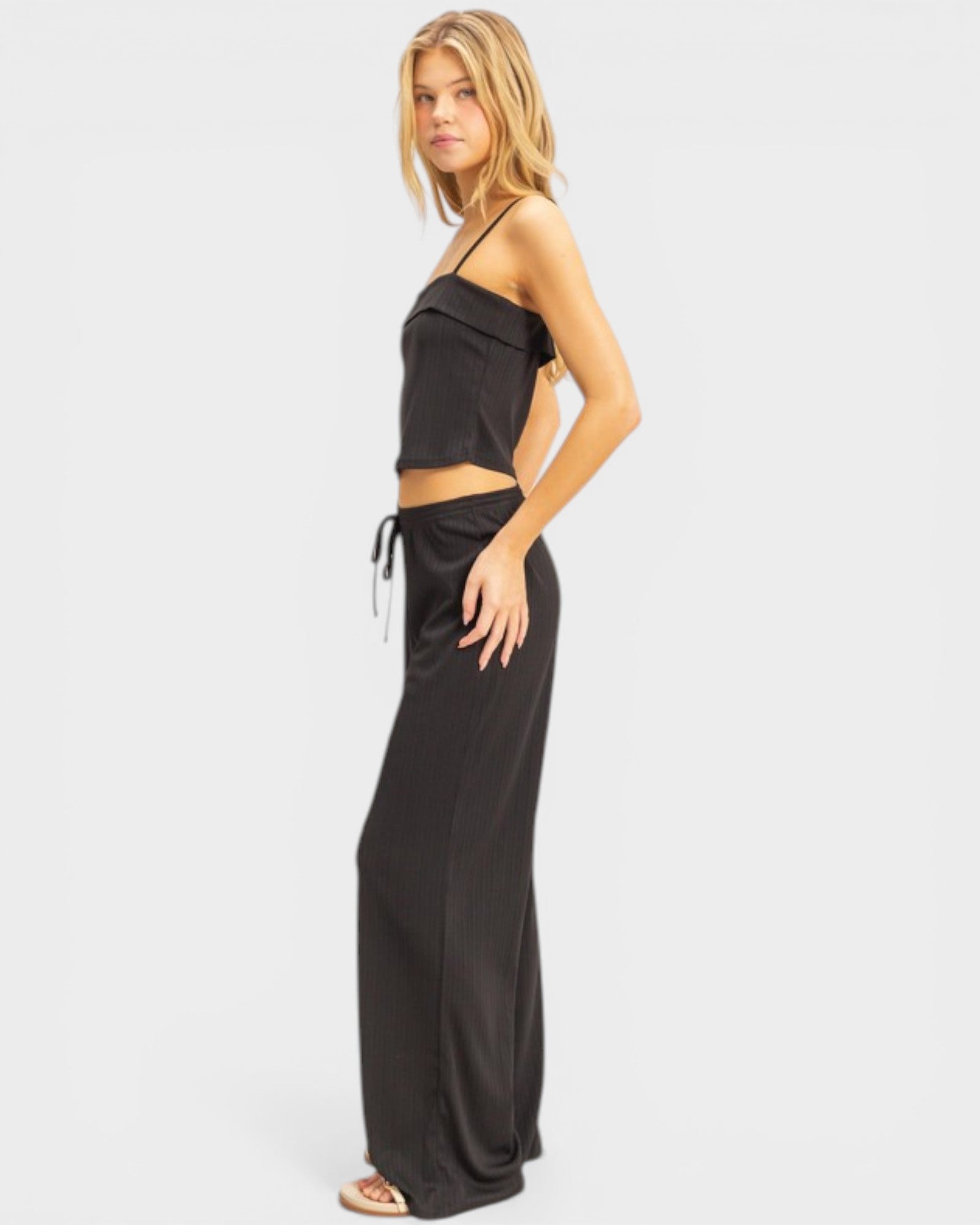 Woman wearing a black strapless top and wide-leg pants on a white background