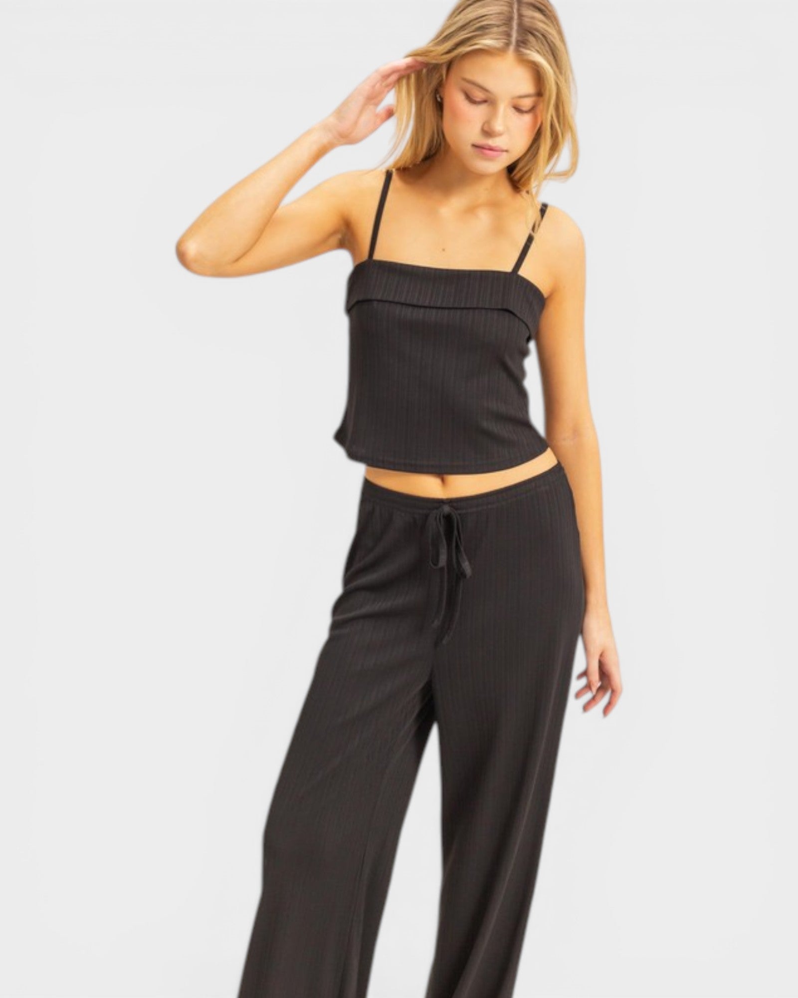 Woman wearing a black ribbed tank top and black high-waisted pants on a light gray background