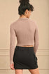 Woman wearing a beige ribbed sweater and black skirt against a beige wall.
