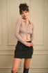 Woman wearing a pink ribbed cardigan and black skirt against a beige wall.