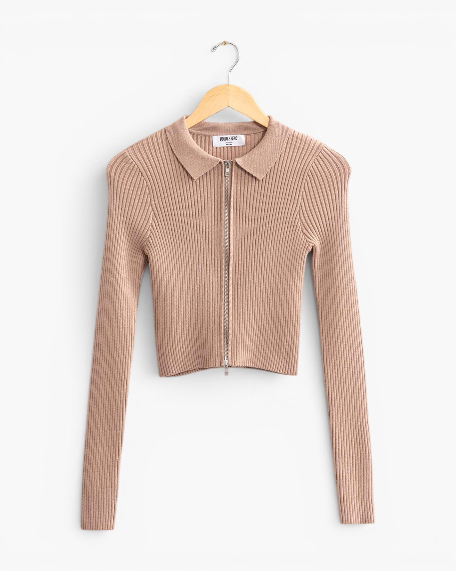A beige ribbed knit long-sleeve crop top with a collar and front zipper, hanging on a wooden hanger against a plain white background.