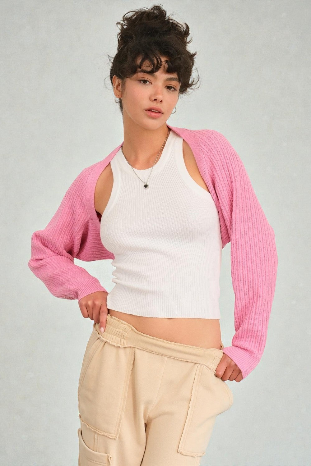 Person wearing a pink cardigan over a white top and beige pants on a gray background