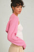 Woman wearing a pink ribbed sweater over a white top on a light gray background