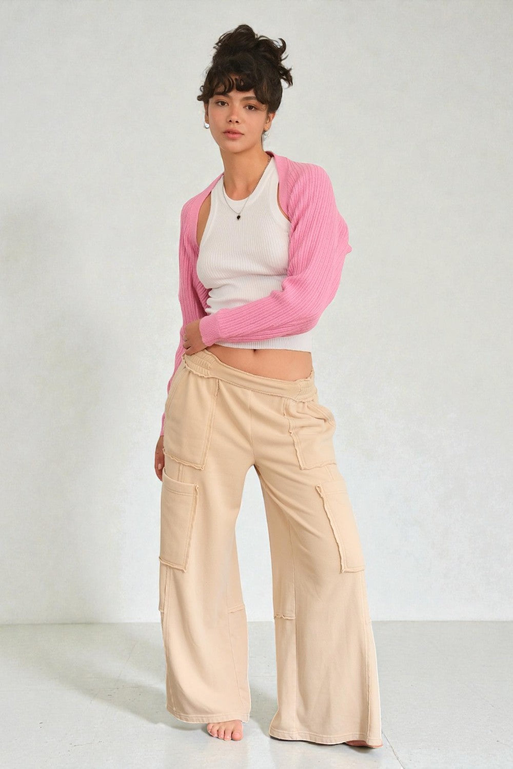 Woman wearing a pink cardigan, white top, and beige pants on a white background