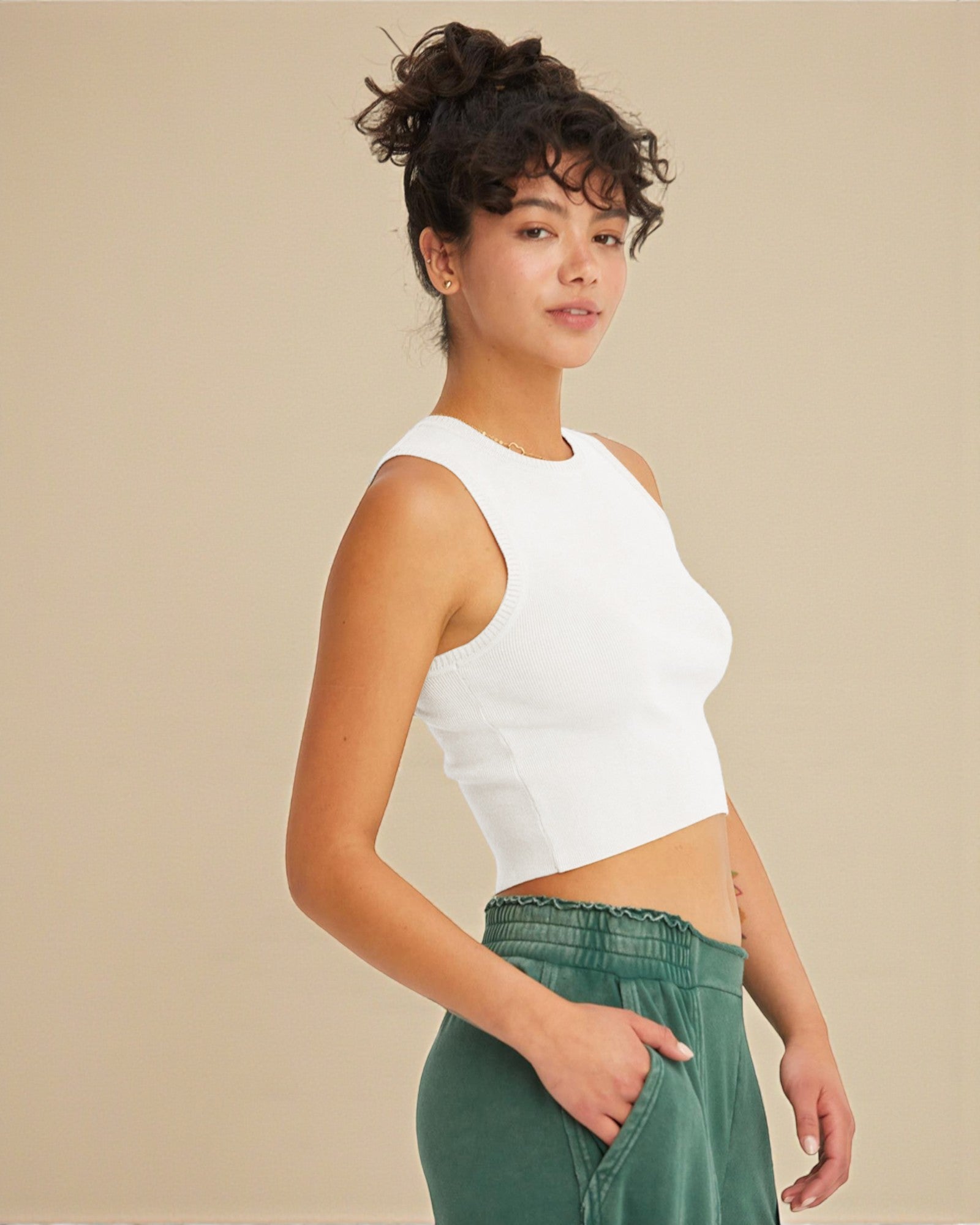 Woman wearing a white sleeveless top and green pants against a beige background