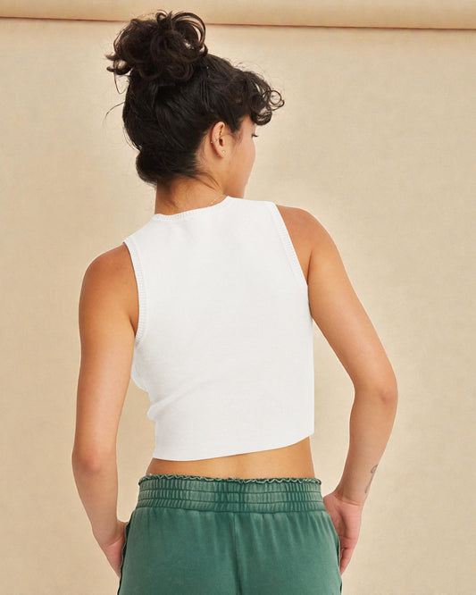 Person wearing a white sleeveless top and green pants against a beige background