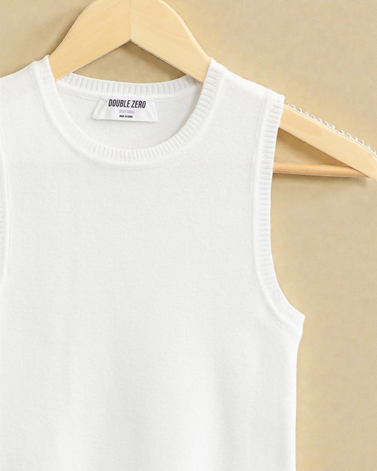 White sleeveless top on a hanger with 'Double Zero' label against a beige background