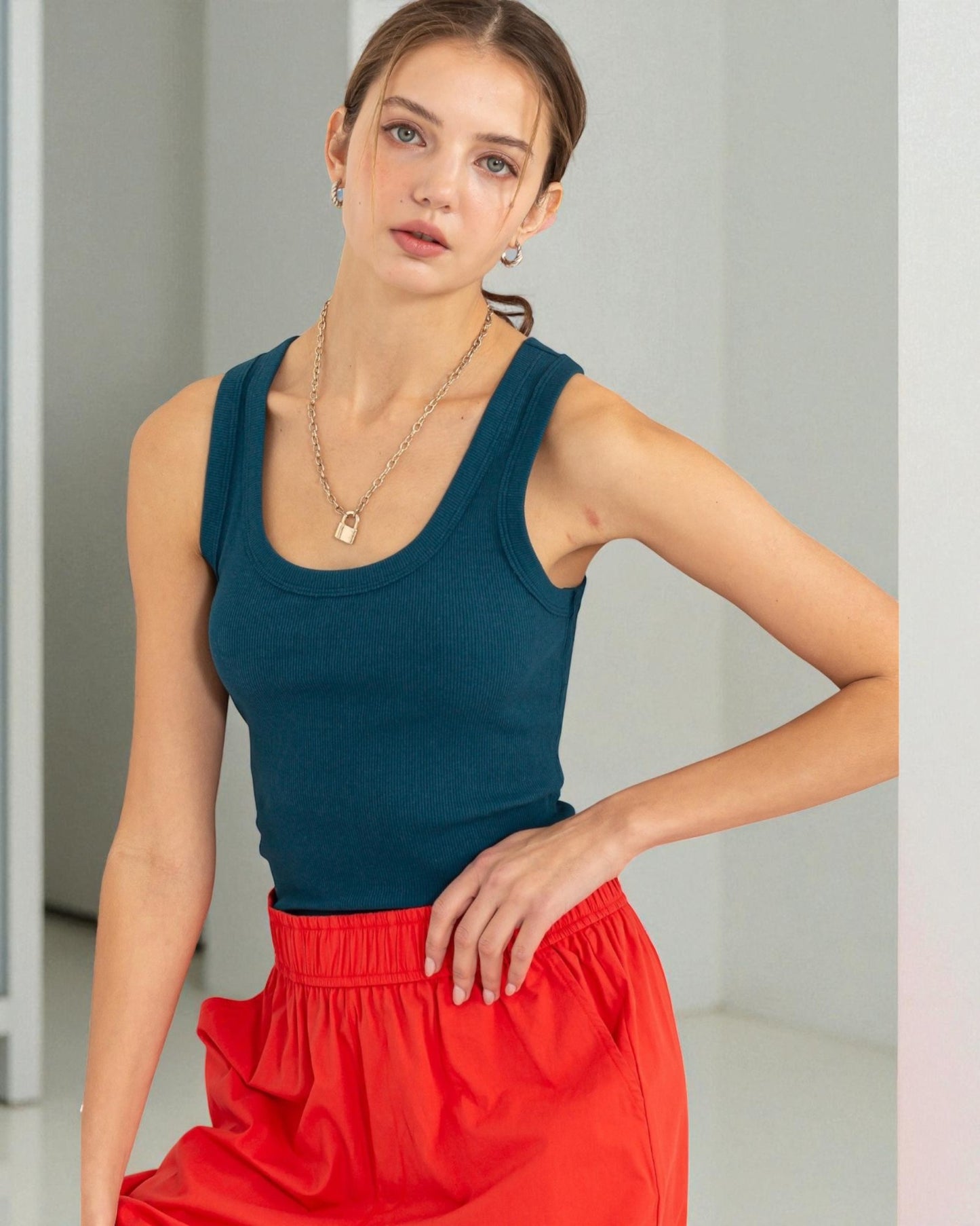 Woman wearing a teal tank top and red pants against a plain background