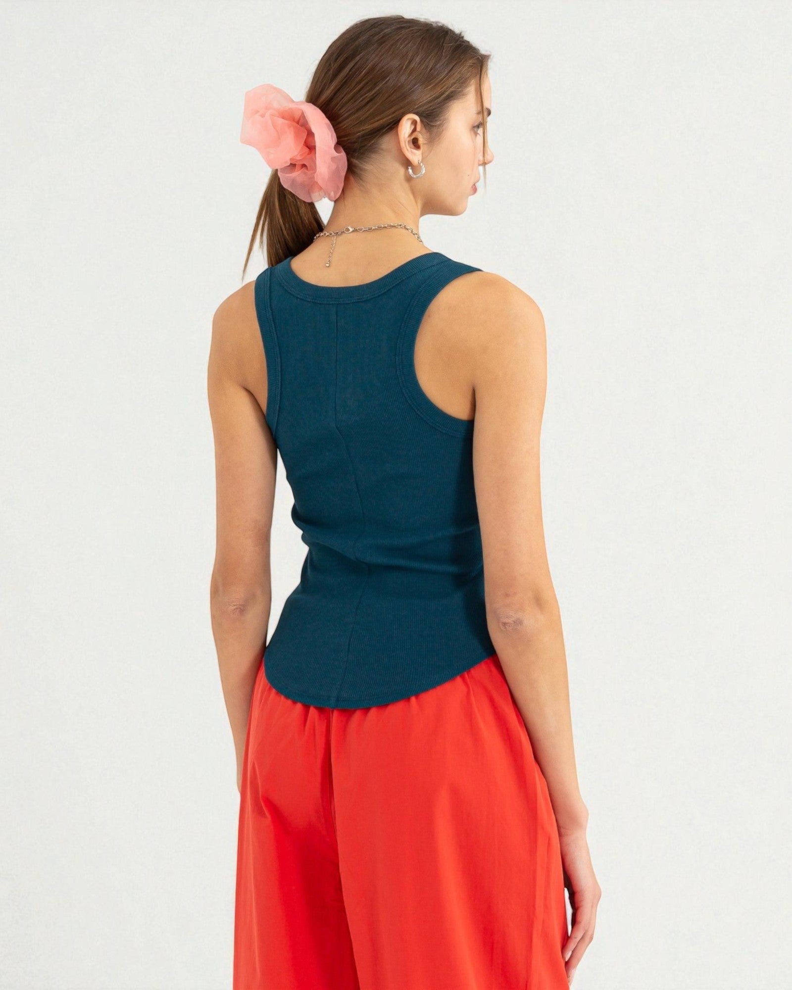 Woman wearing a teal sleeveless top and red pants on a white background