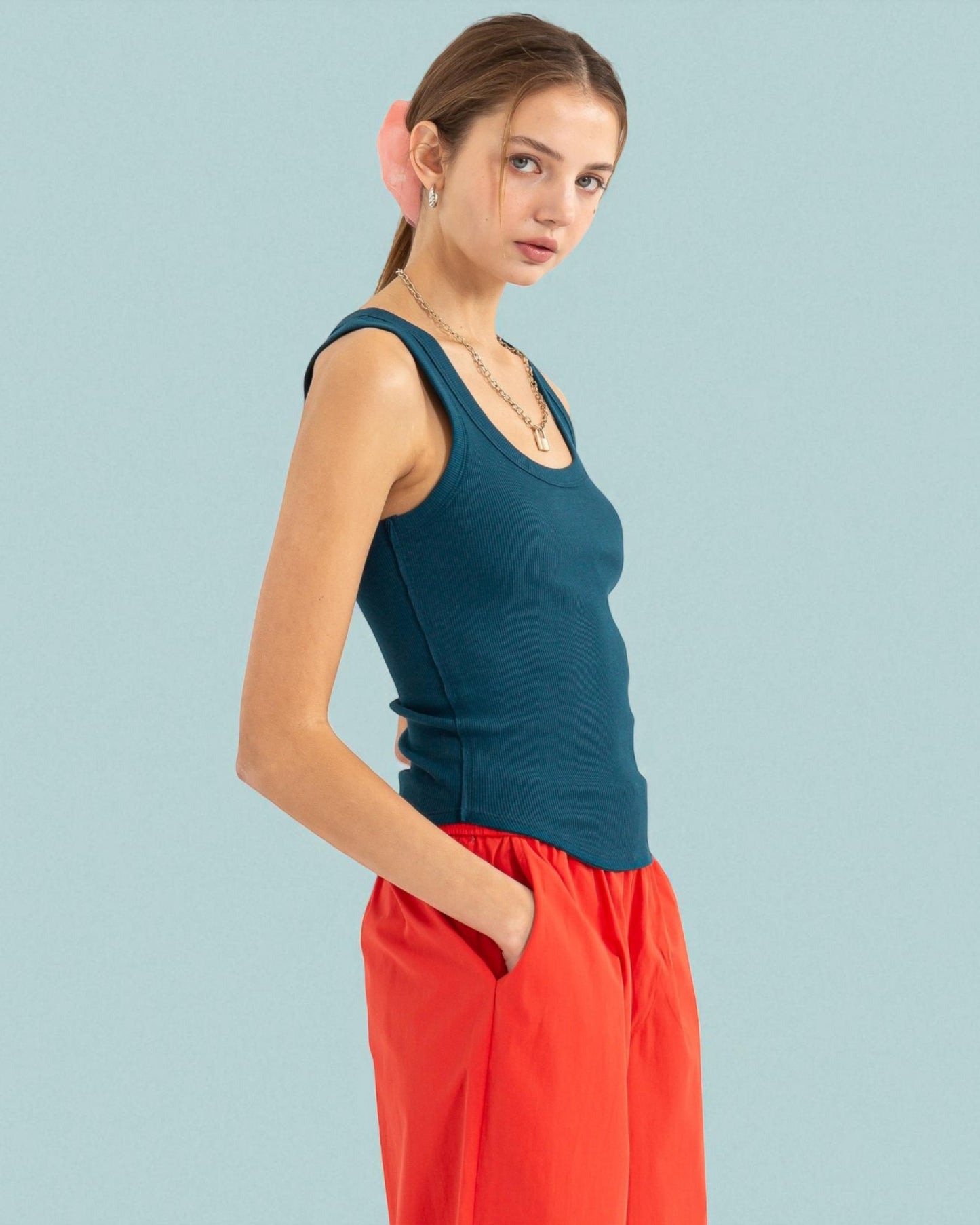 Woman wearing a teal tank top and red pants against a light blue background