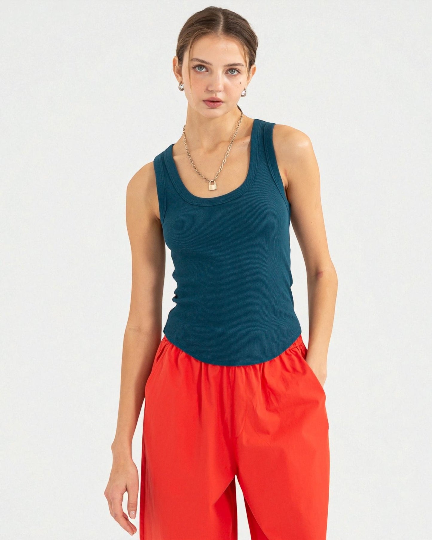 Woman wearing a teal tank top and red pants on a white background