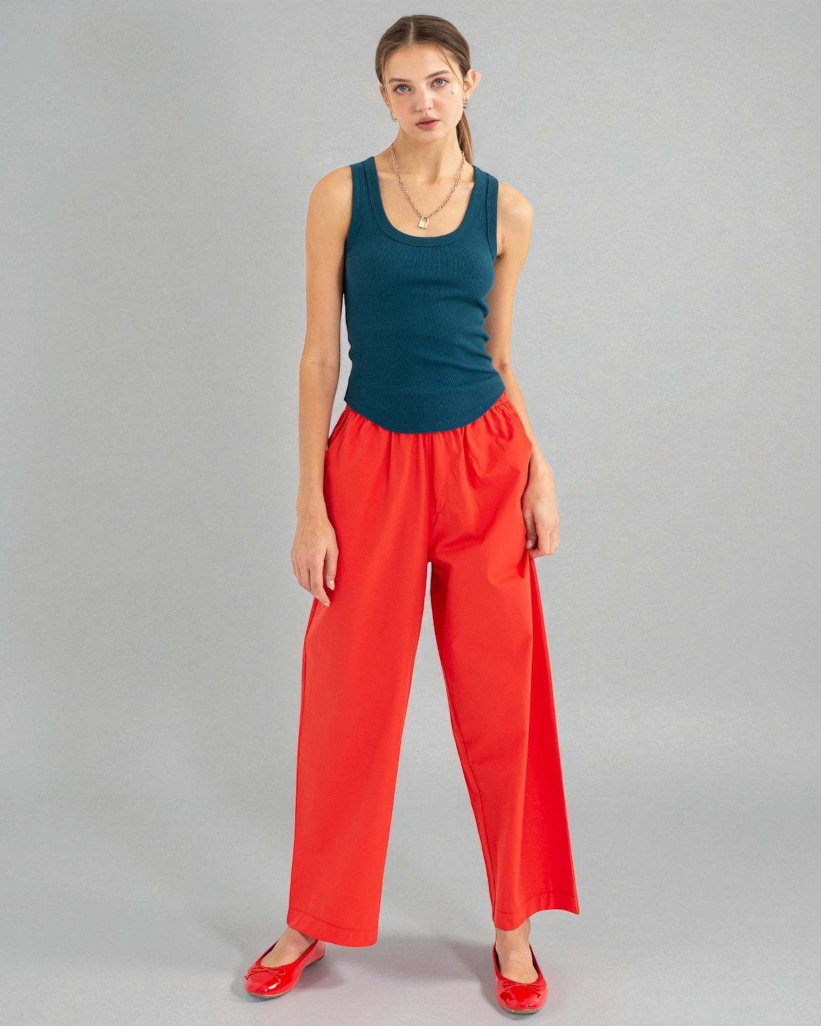 Woman wearing a teal tank top and red pants on a gray background