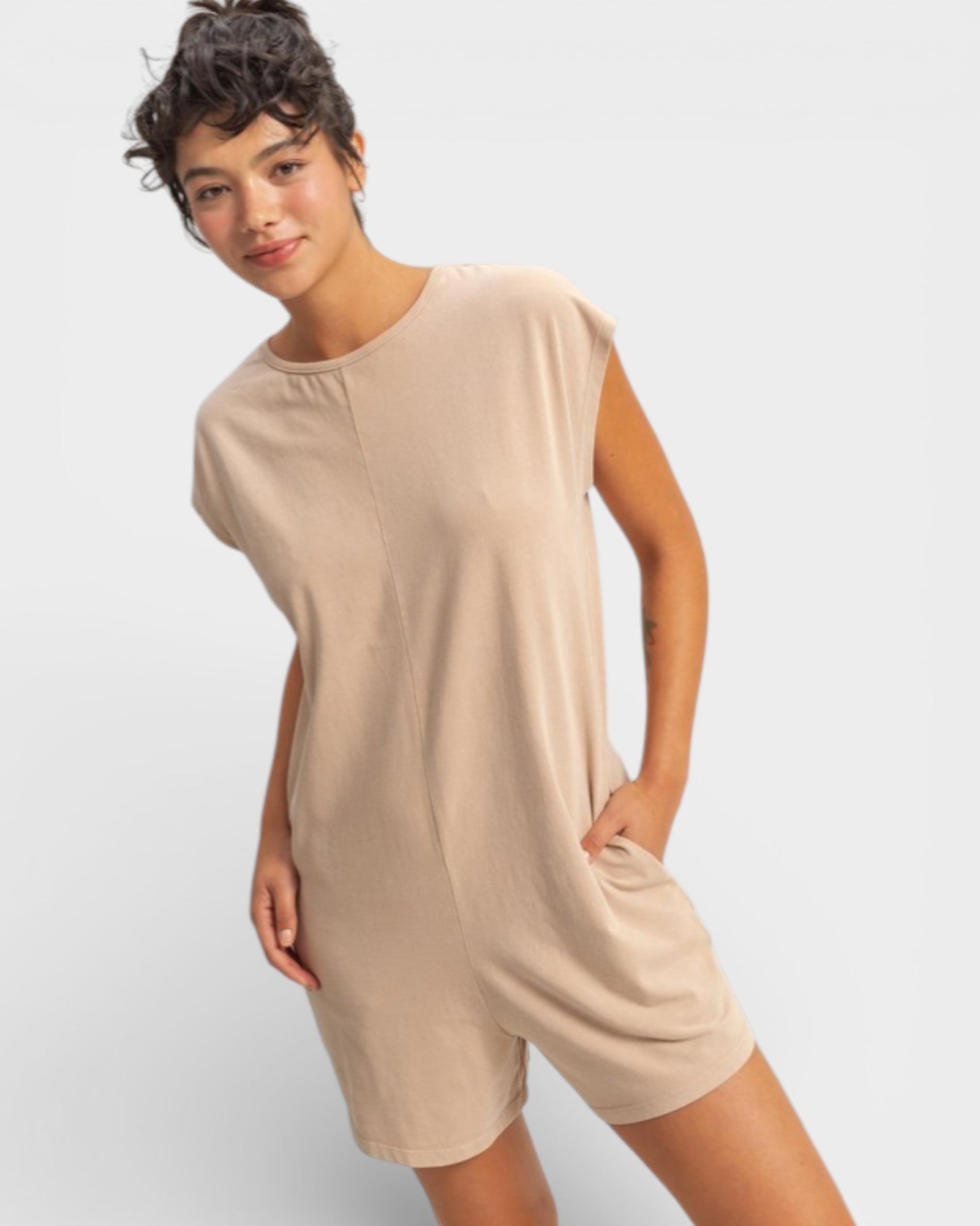Woman wearing a beige sleeveless dress with shorts on a light gray background