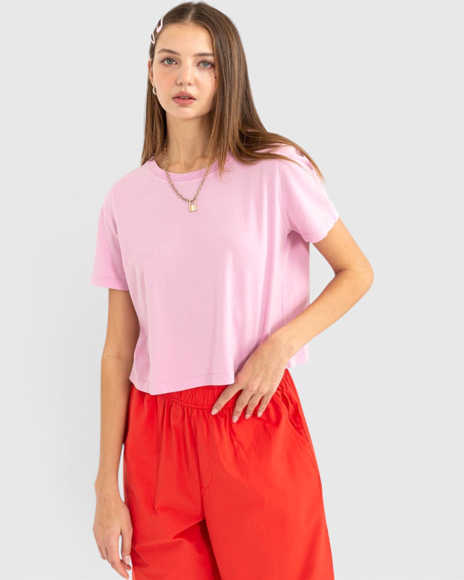 Woman wearing a pink top and red pants on a light gray background