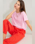 Woman wearing a pink top and red pants sitting on a light gray background