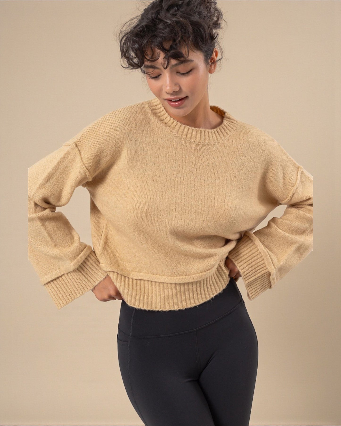Woman wearing a beige sweater and black pants against a beige background