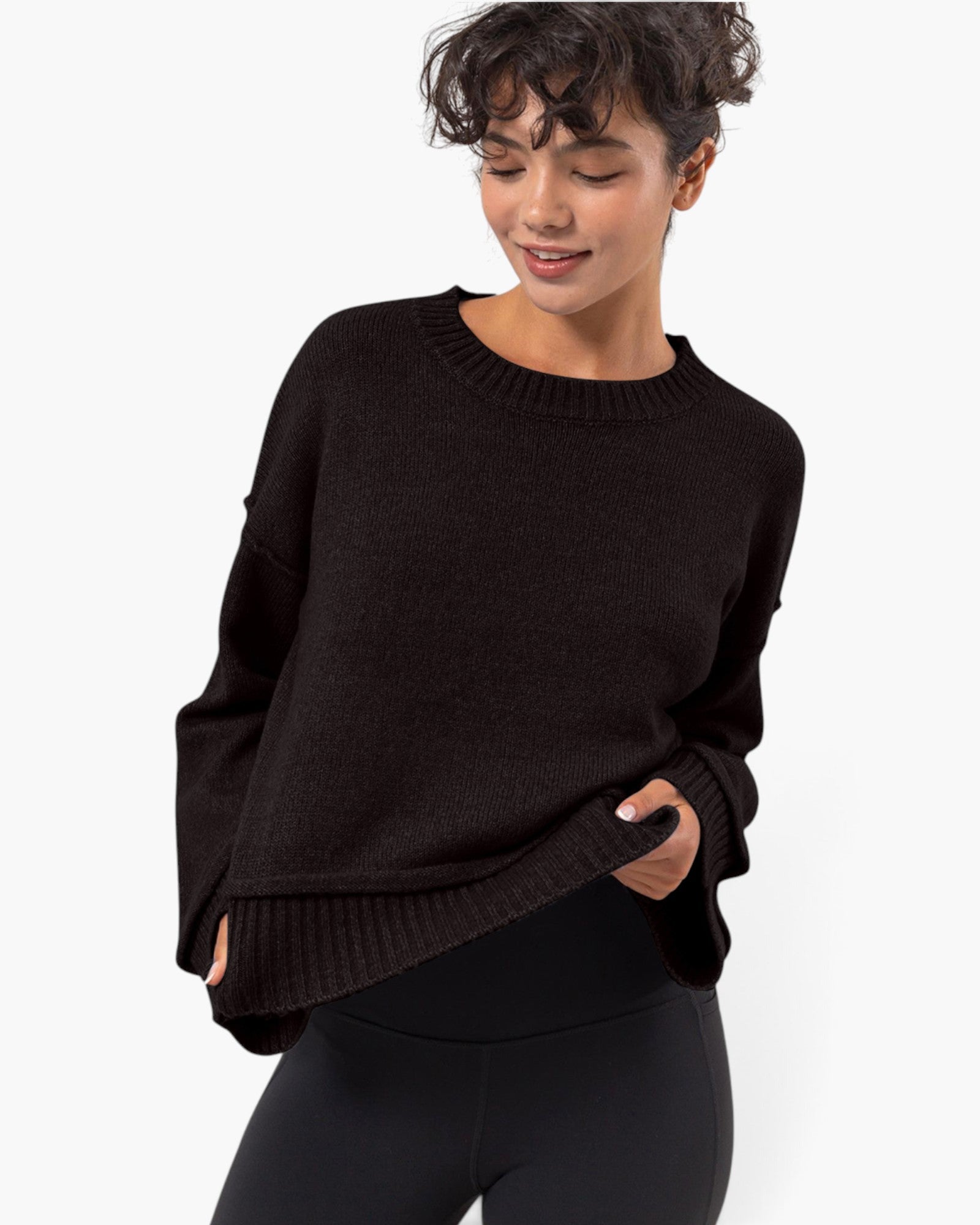 A woman wearing a dark brown knit crewneck sweater and black leggings, photographed against a clean white studio background.