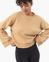 A woman wearing a cropped, long-sleeve knit sweater in a warm camel beige color, paired with black leggings, against a clean white background.
